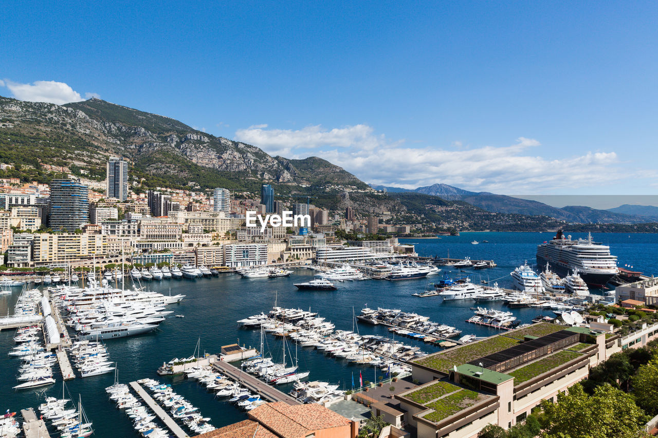 HIGH ANGLE VIEW OF SAILBOATS MOORED ON SEA AGAINST BUILDINGS