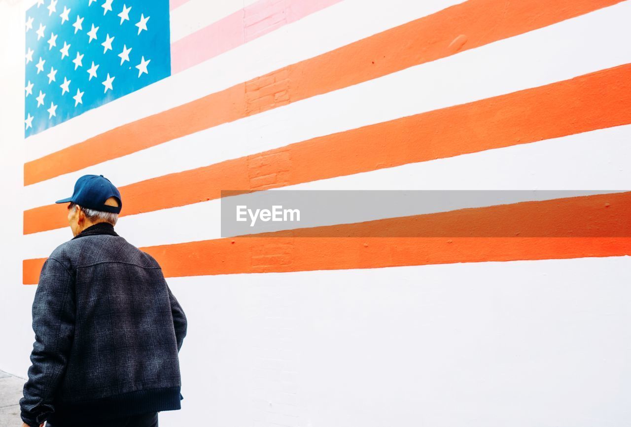 Rear view of man walking by american flag painted on wall