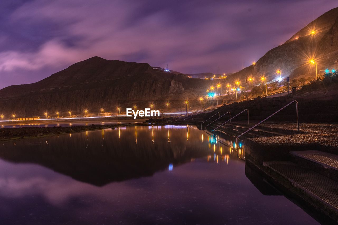 Reflection of illuminated mountain in natural swimming pool at the sea with sky at night