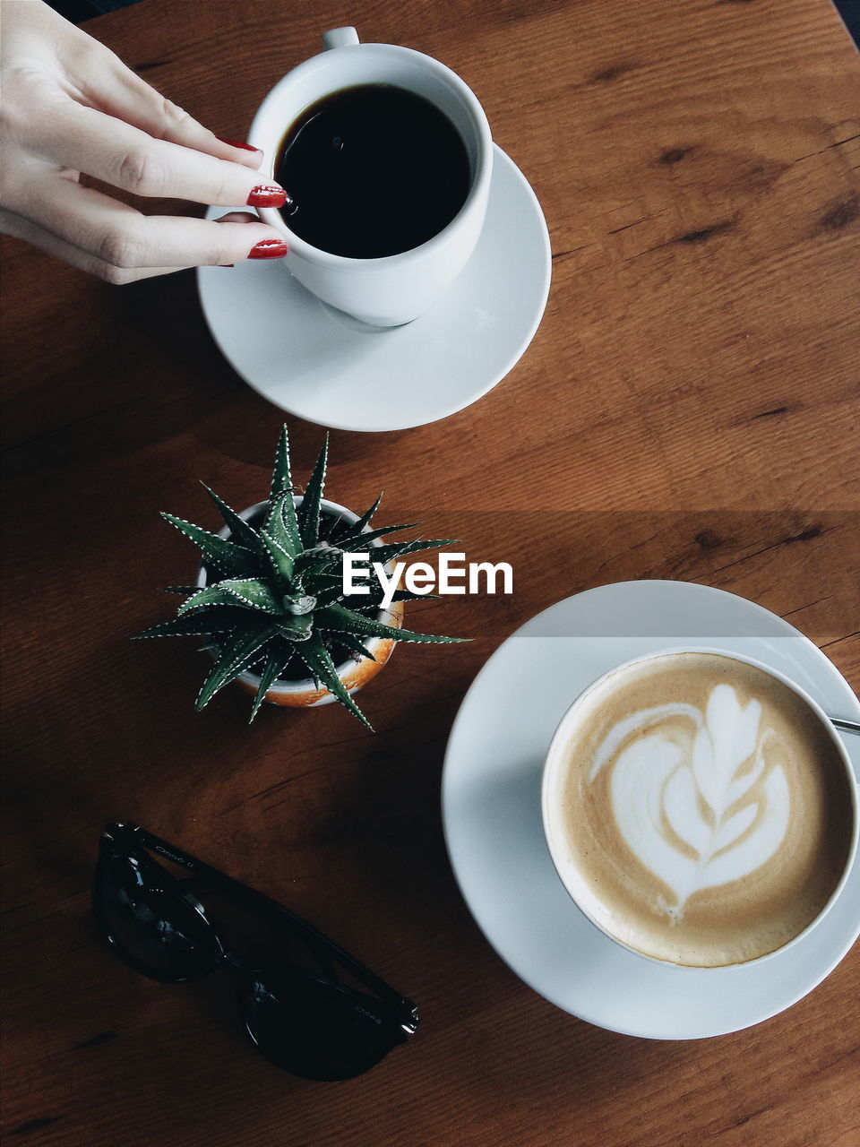 Cropped image of woman hand on coffee by potted cactus on table