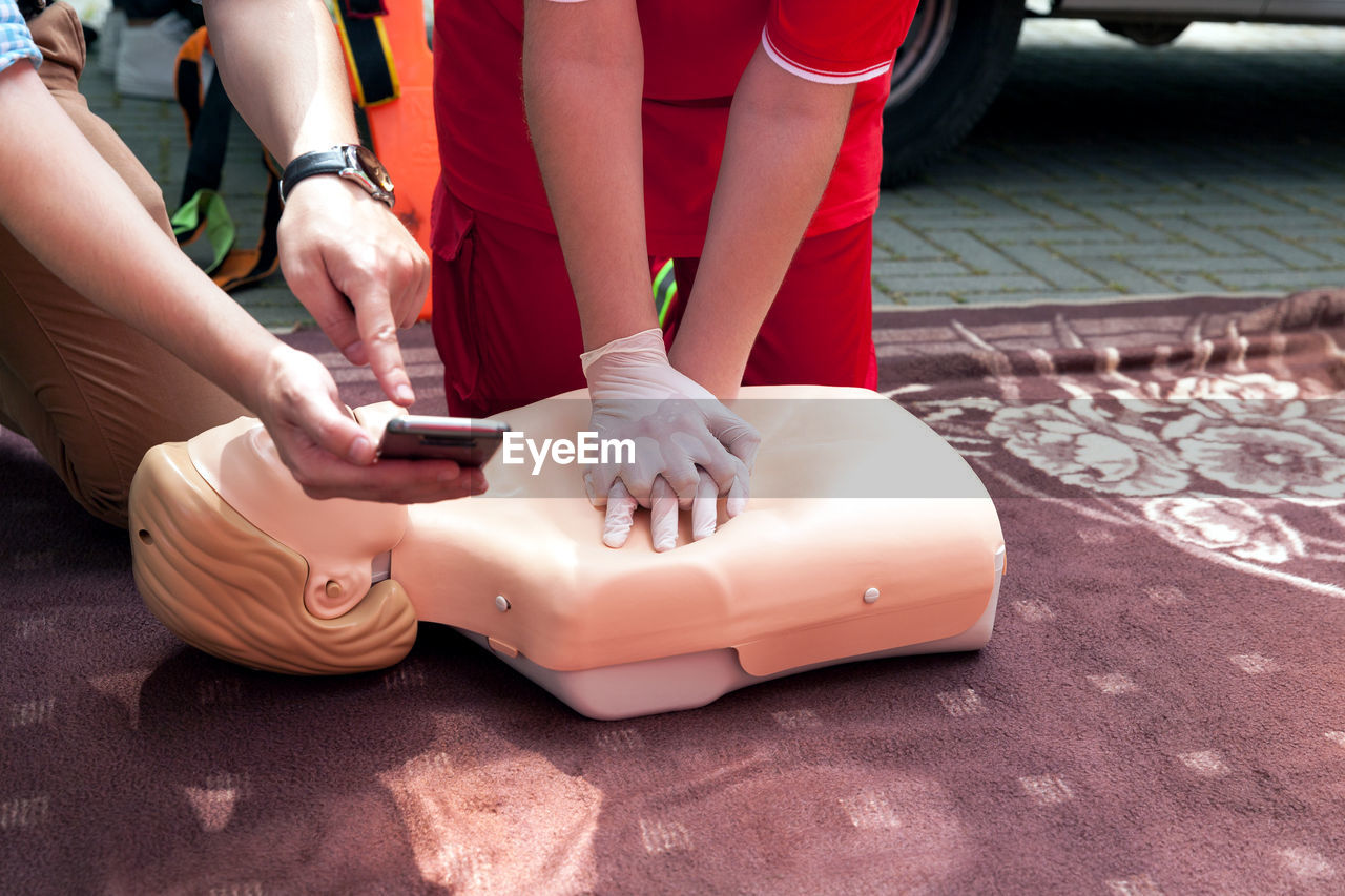 Midsection of man showing phone to woman practicing on cpr dummy