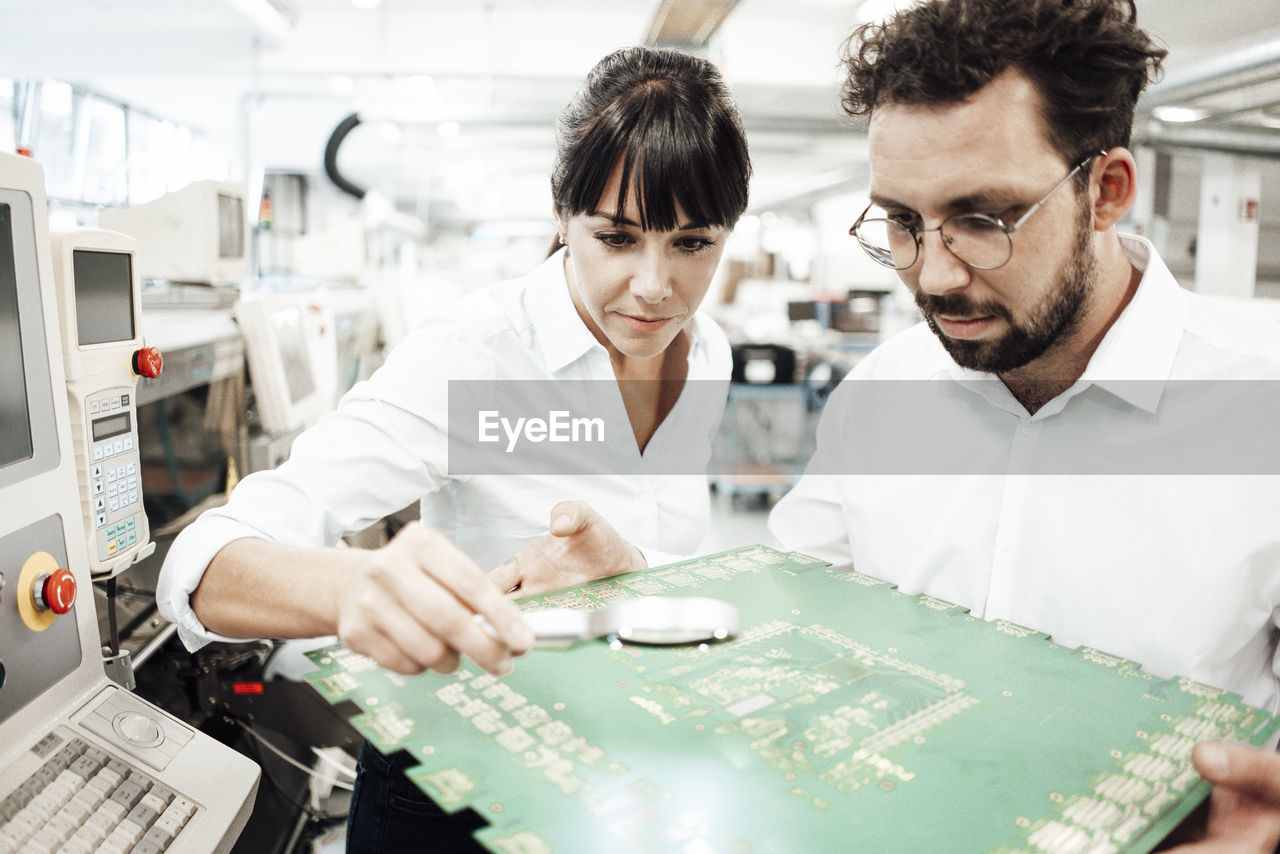 Businesswoman and businessman analyzing large computer chip with magnifying glass in industry