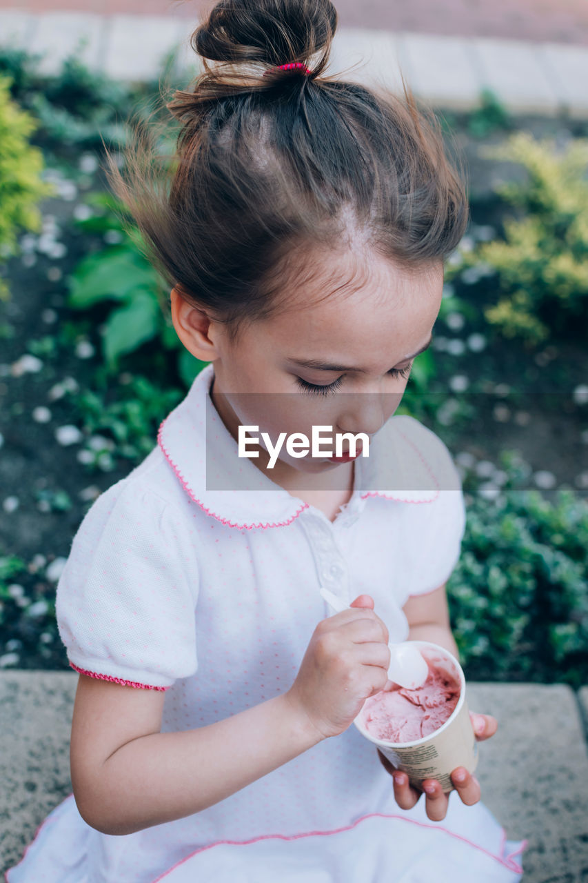 High angle view of cute girl holding ice cream while sitting outdoors