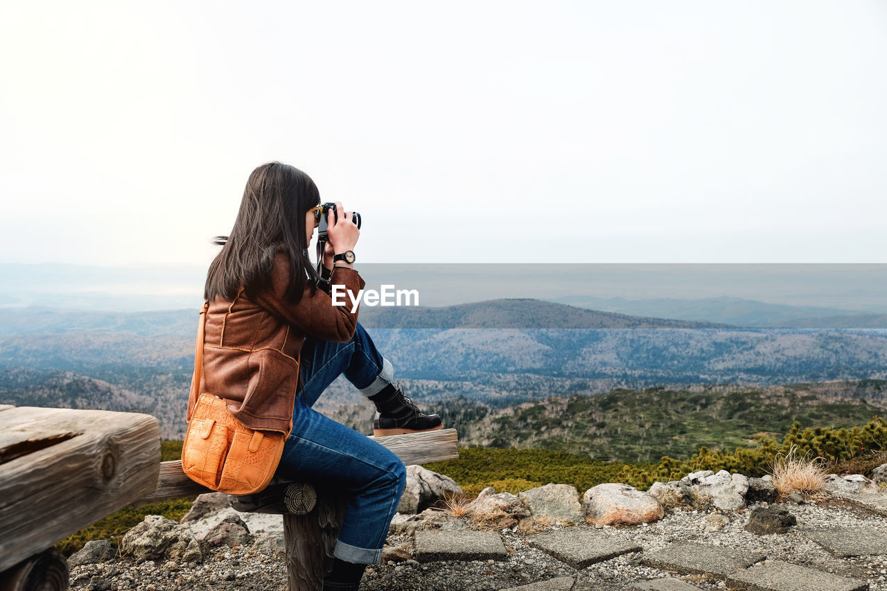 Woman photographing on mountain against clear sky