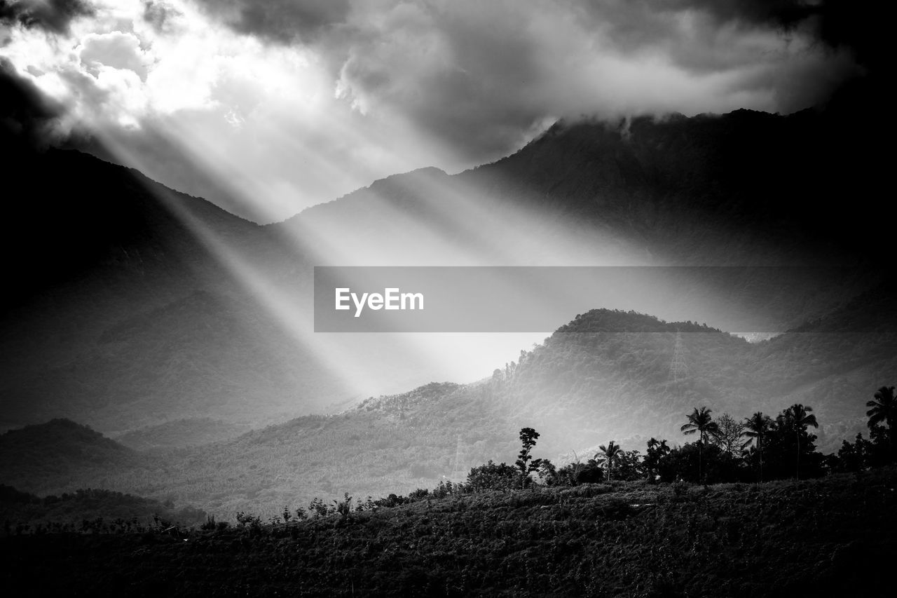 Scenic view of mountains against sky with sunlight bursting through