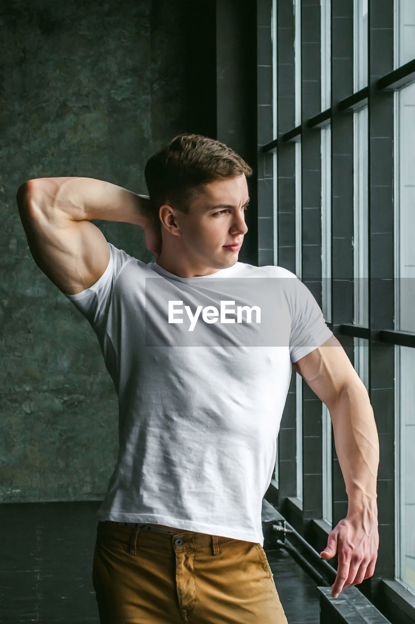 Muscular man standing by window at home