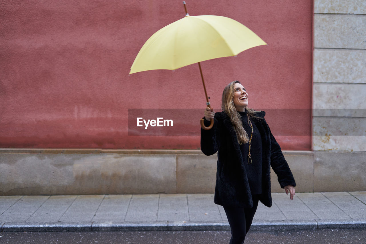 Pretty girl plays in the street with her yellow umbrella while laughing.