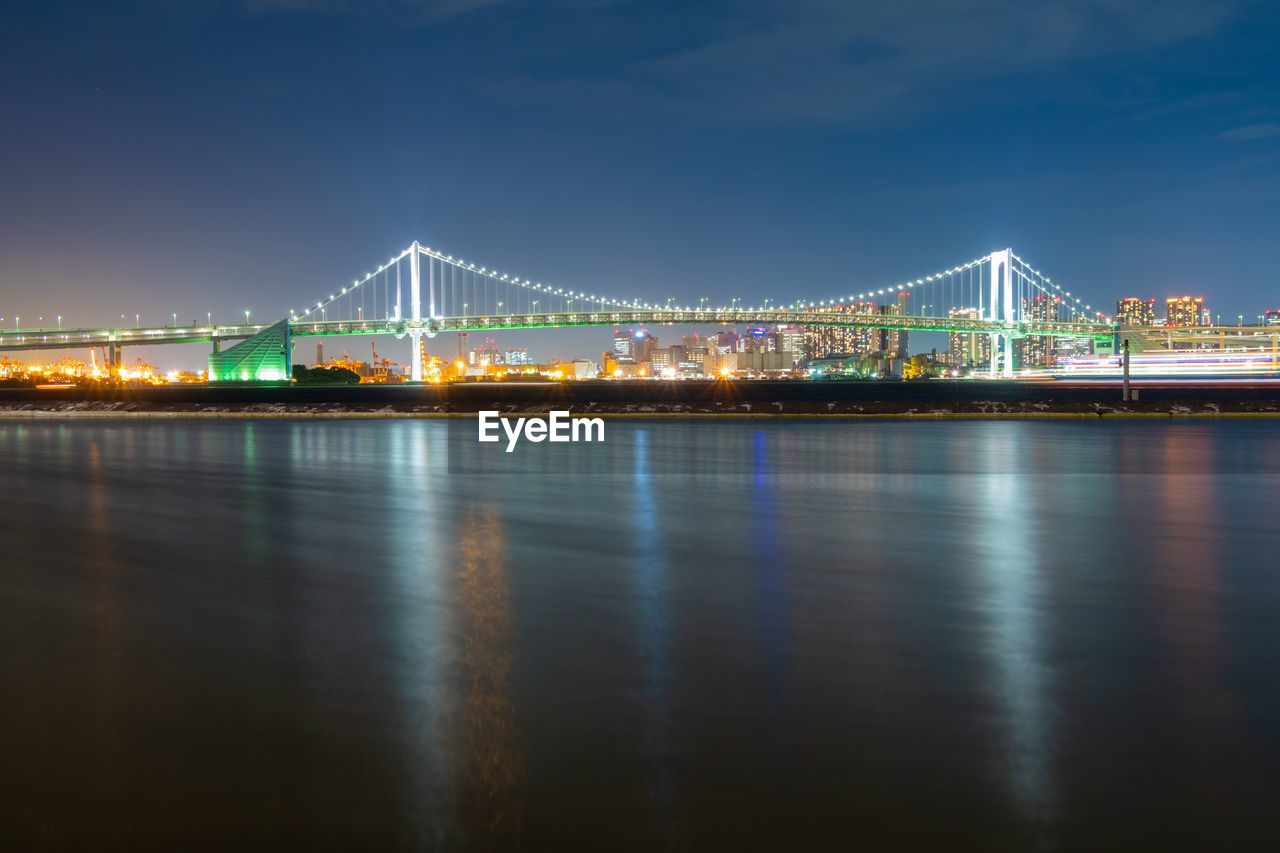 ILLUMINATED BRIDGE OVER RIVER AGAINST SKY