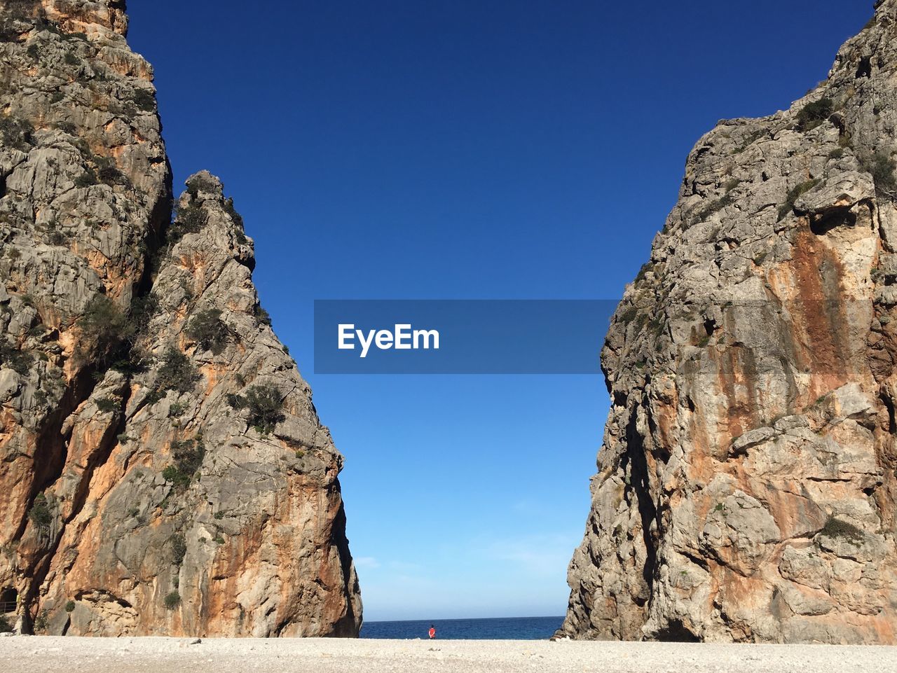 Rock formations by sea against clear blue sky