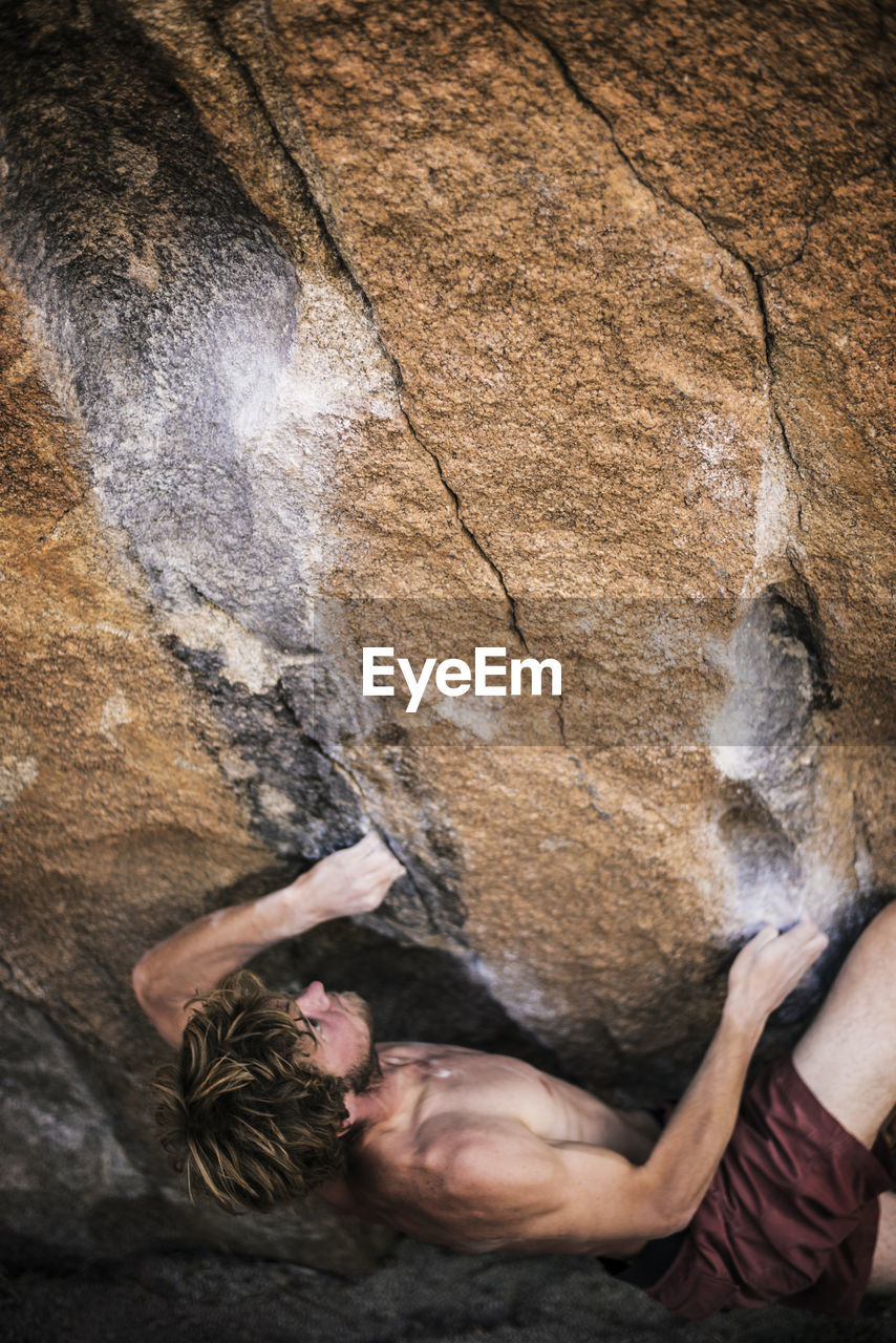 High angle view of shirtless man climbing rock