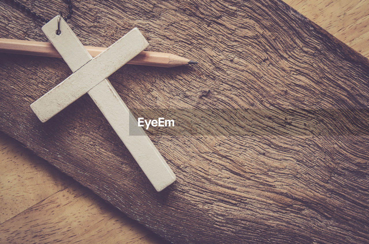 High angle view of cross and pencil on wood
