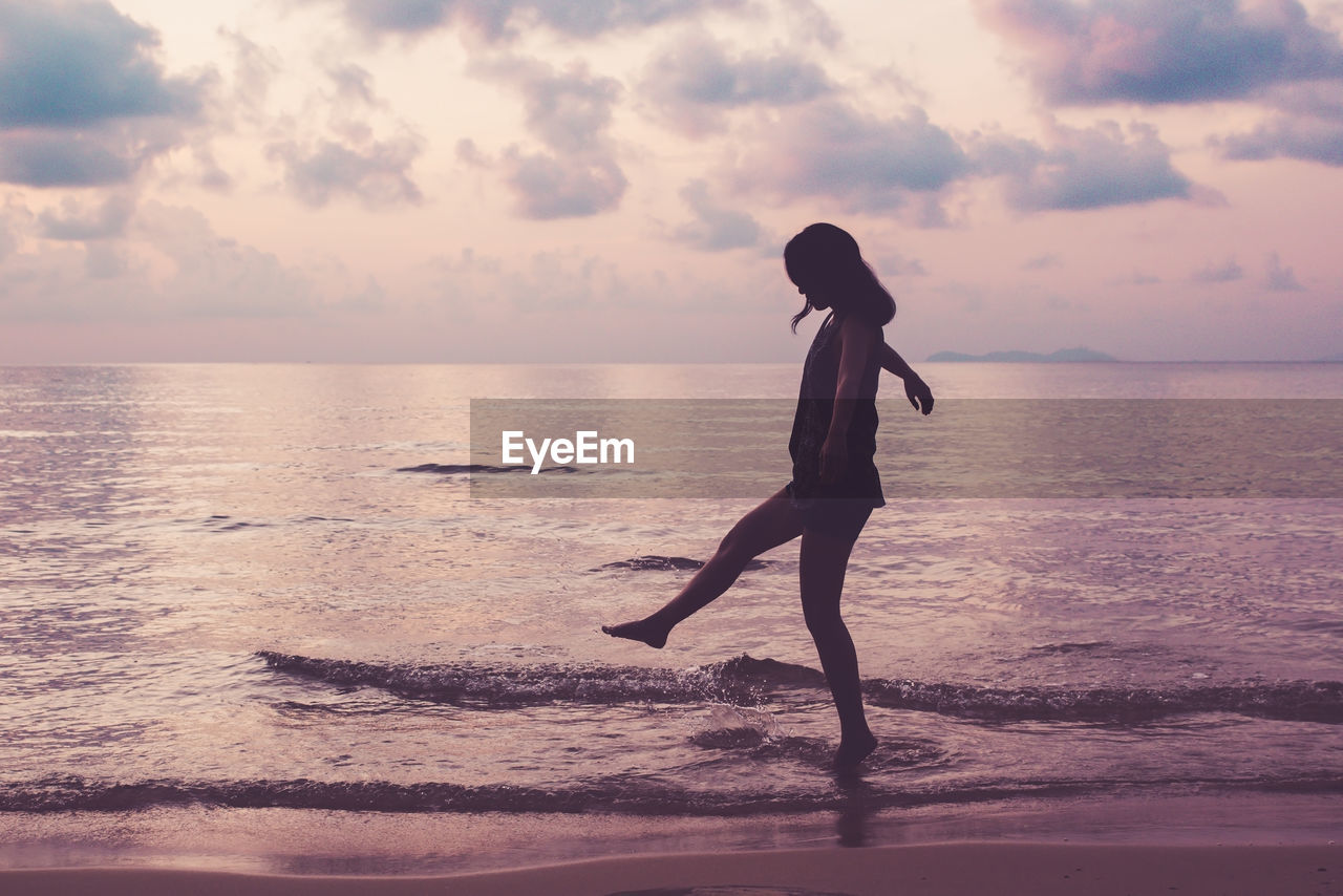 Side view of woman on shore at beach against sky during sunset