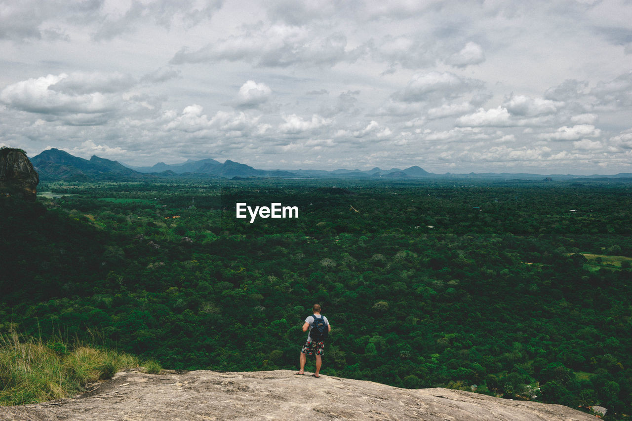 REAR VIEW OF MAN LOOKING AT MOUNTAINS AGAINST SKY