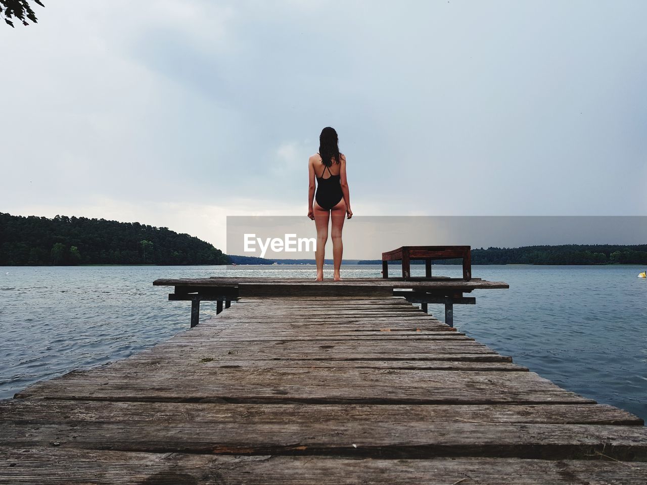 Rear view of teenage girl standing on pier over lake against sky