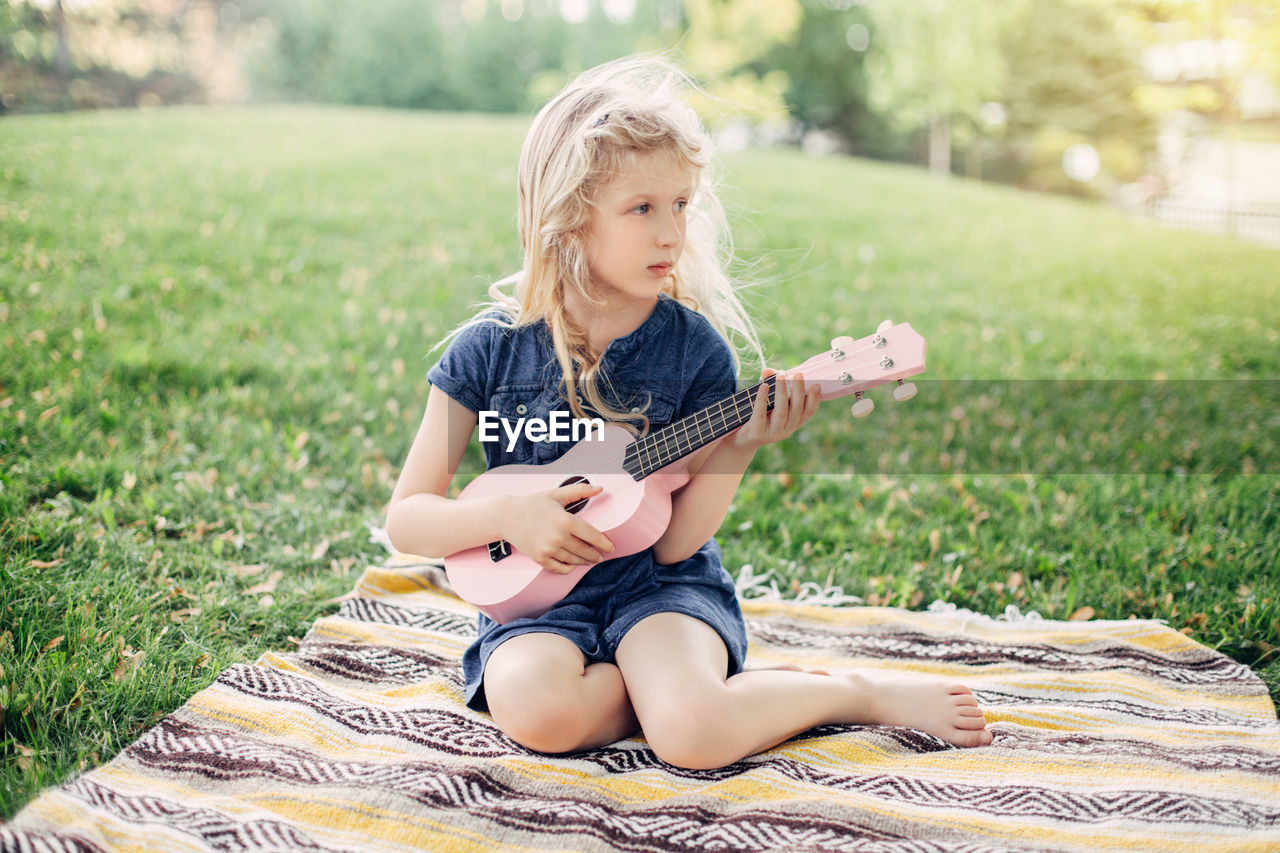 Cute adorable blonde girl playing pink guitar toy outdoor. child playing music and singing song 