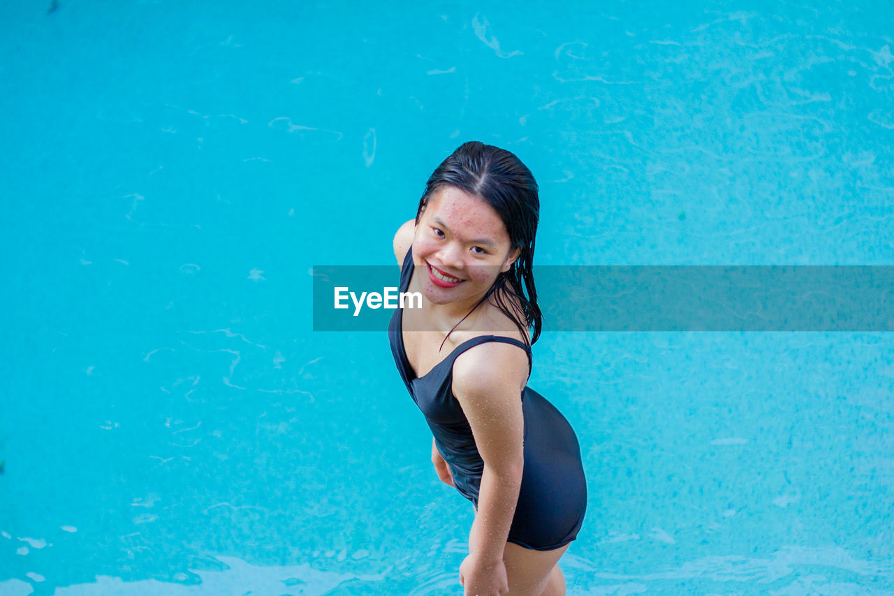 Beautiful asian woman smiling standing up at pool side on sunny day