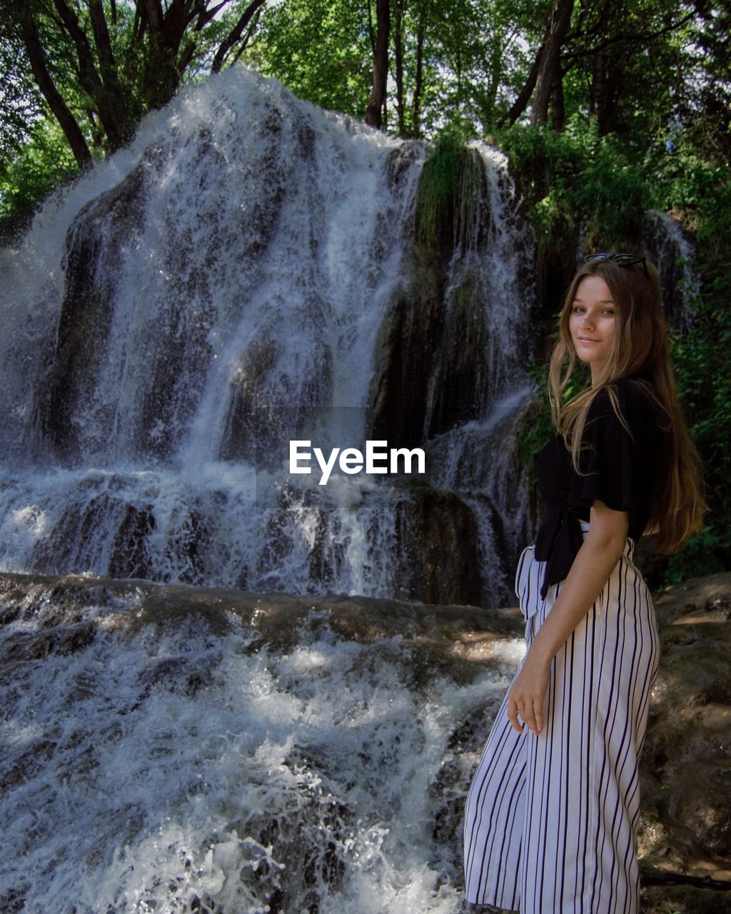 YOUNG WOMAN STANDING BY WATERFALL