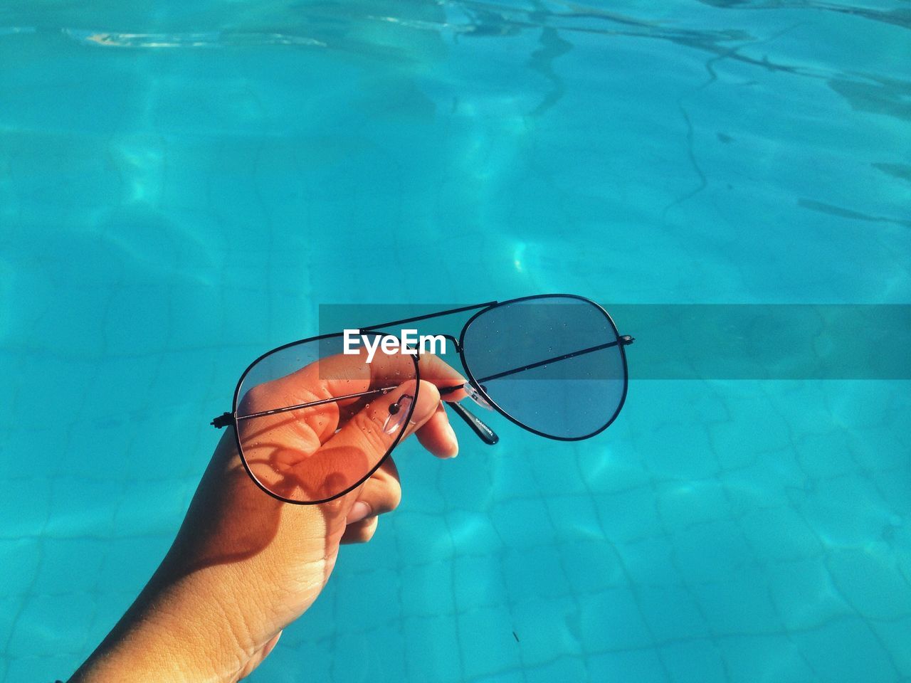 Close-up of person holding sunglasses against swimming pool
