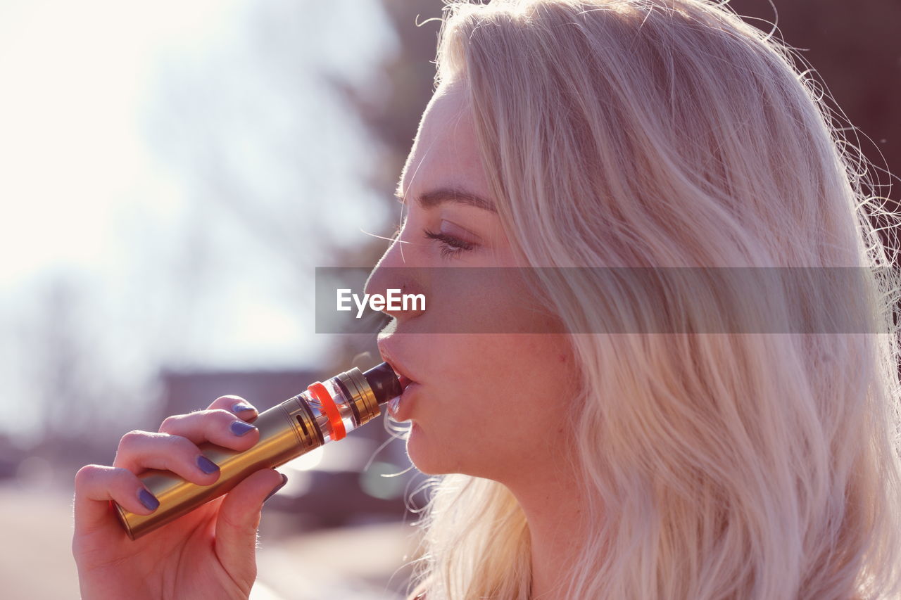 Close-up of young woman with blond hair smoking electronic cigarette