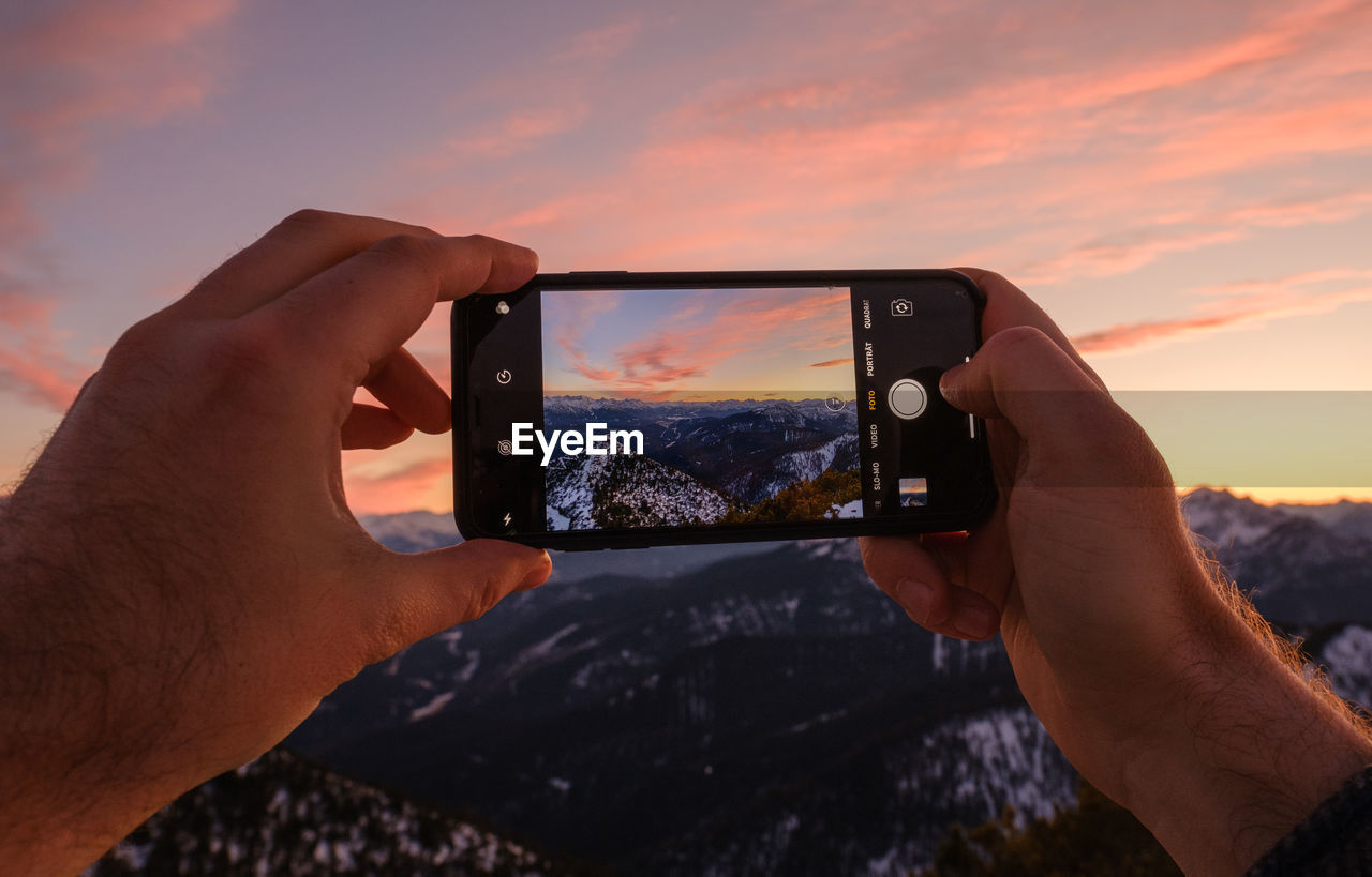 Man photographing with mobile phone against sky during sunset