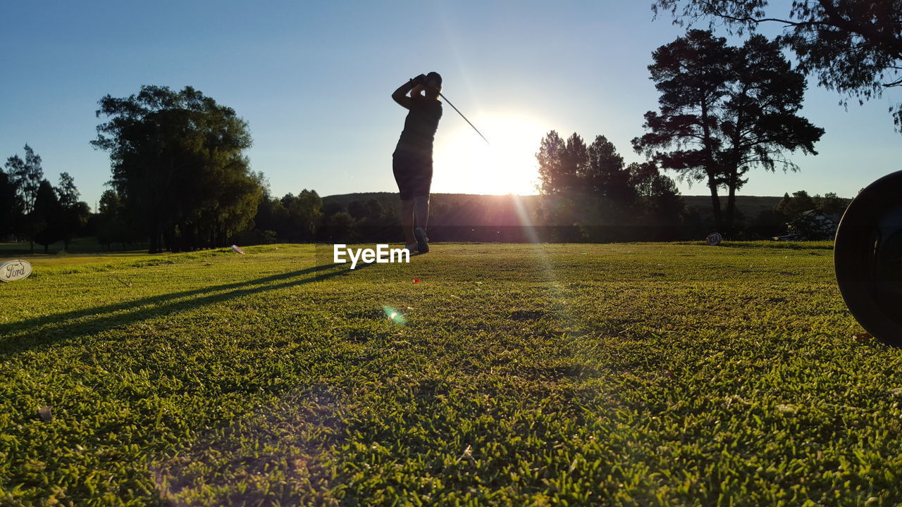 Low angle view of woman at golf course against sky during sunny day