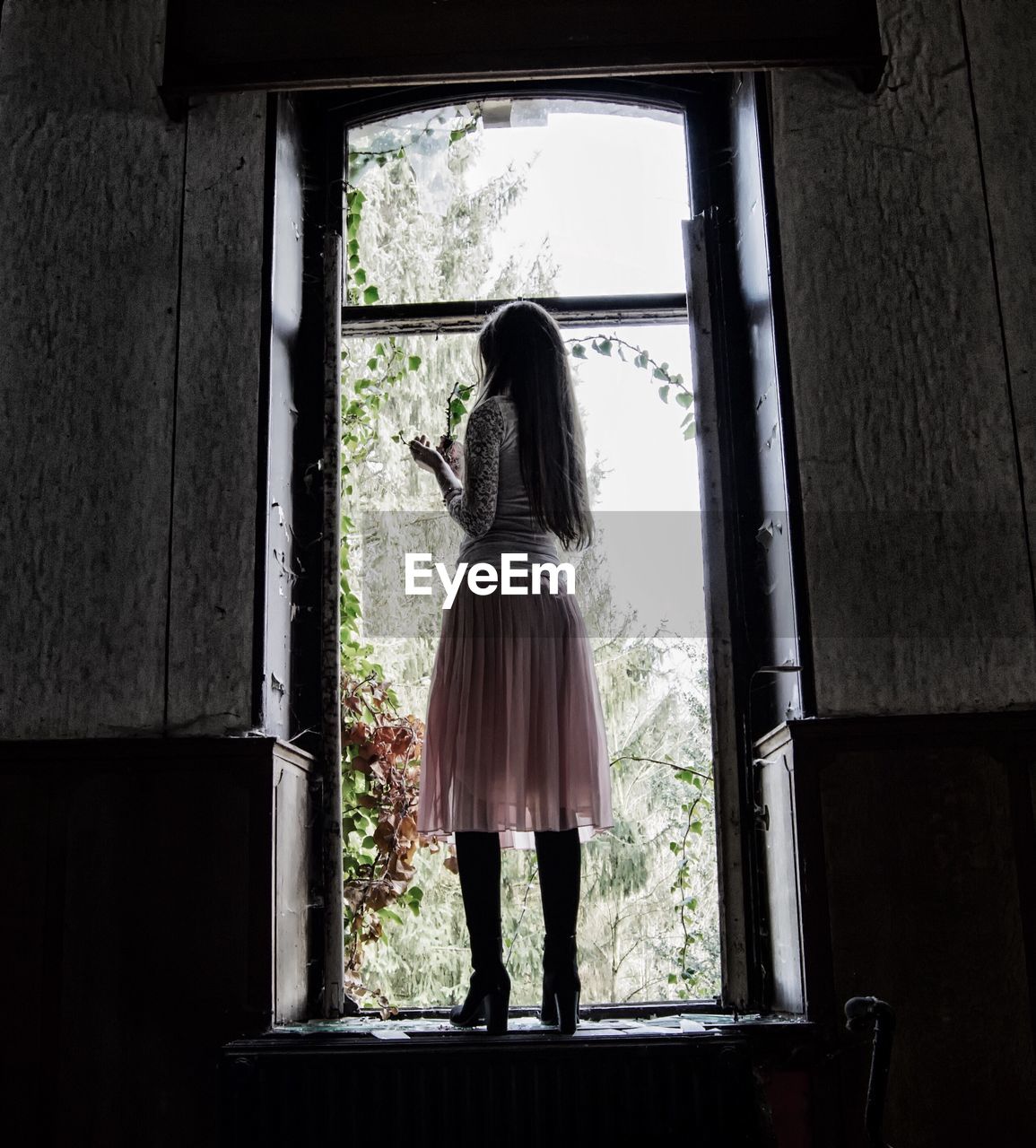 Full length rear view of woman standing on window sill