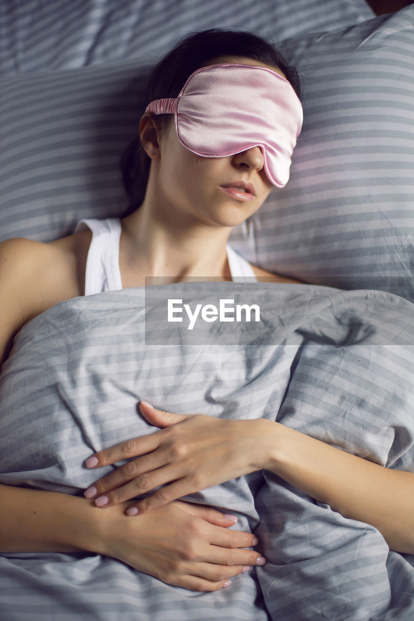 Woman in a pink eye mask lies under a blanket in a bed and suffers from insomnia 