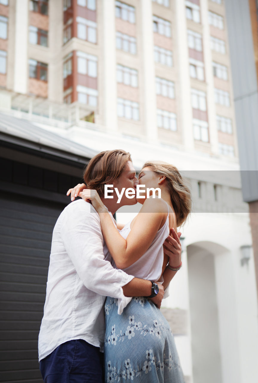 Couple kissing and embracing while standing together on city street. portrait of romantic model