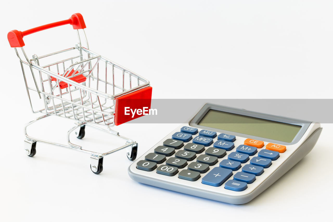 High angle view of shopping cart with calculator on white background