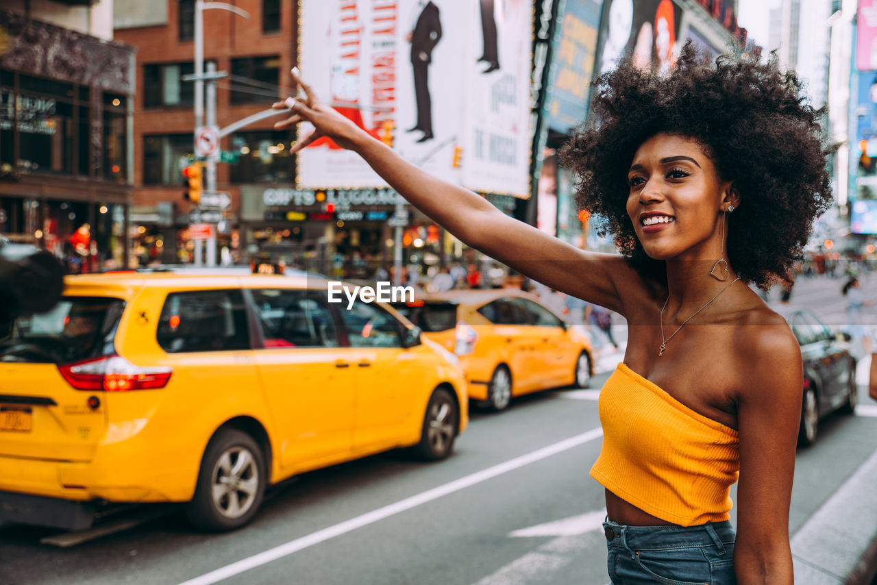 Happy young woman with afro hairstyle hailing a ride on city street