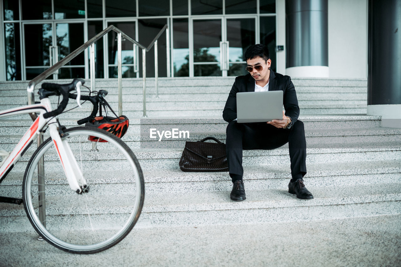 FULL LENGTH OF MAN USING MOBILE PHONE WHILE SITTING ON SEAT AT OFFICE