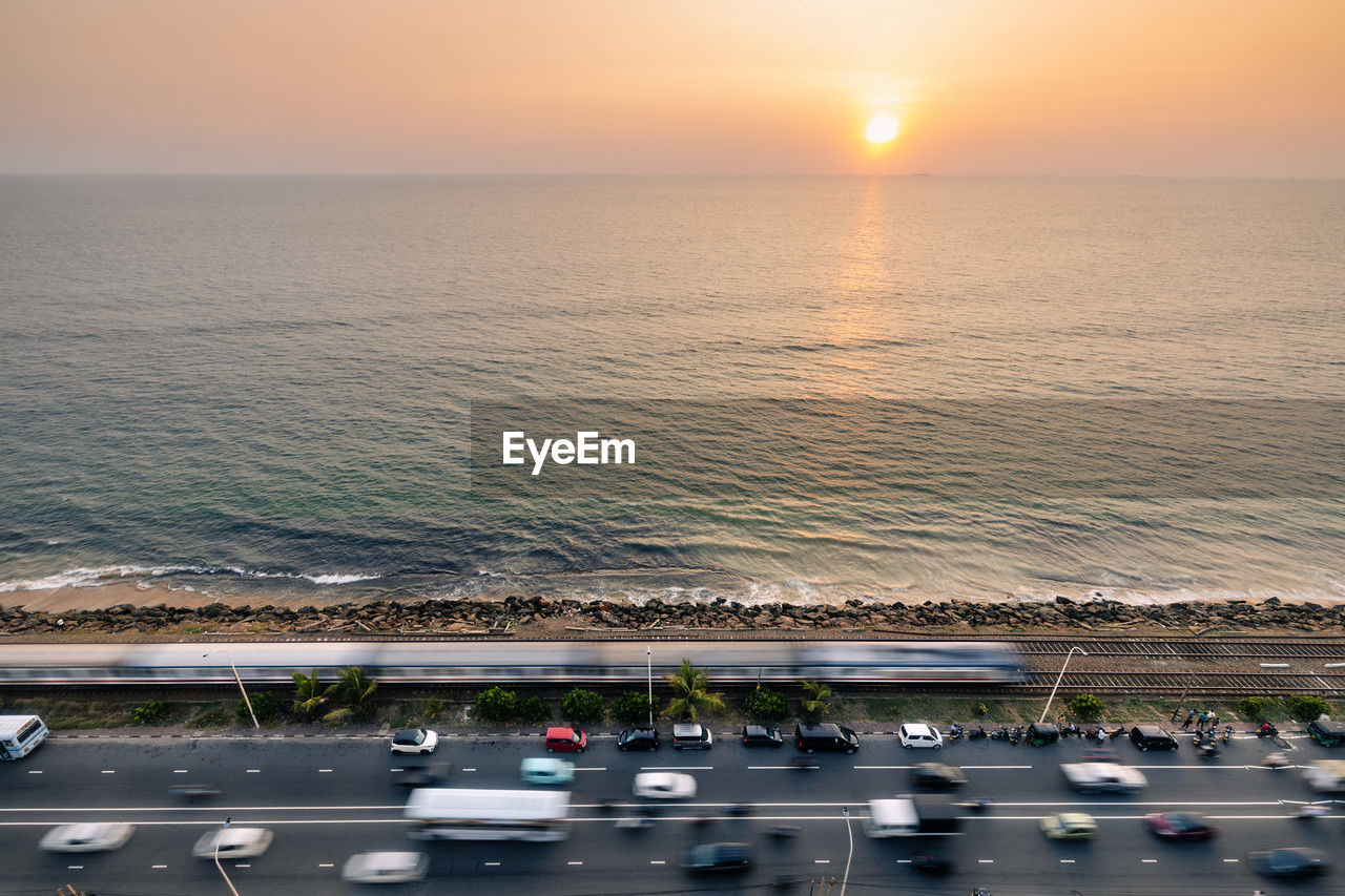 Road and railway track along coast at sunset over ocean. train arriving in colombo, sri lanka.