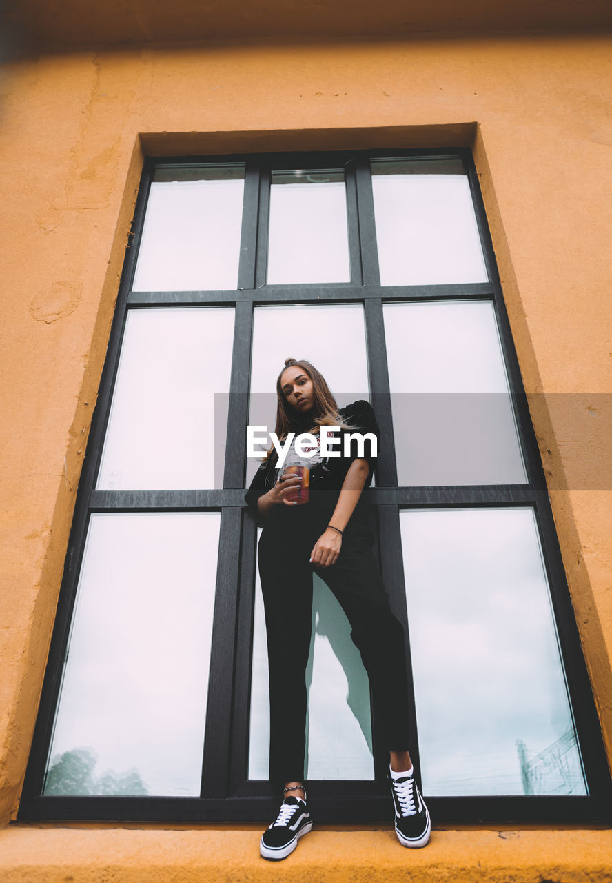 FULL LENGTH PORTRAIT OF WOMAN STANDING BY WINDOW AT HOME