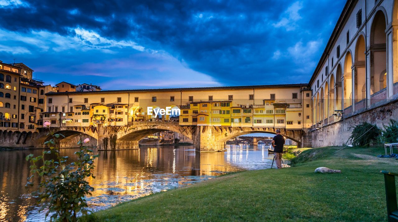 Low angle view of ponte vecchio over arno river against cloudy sky