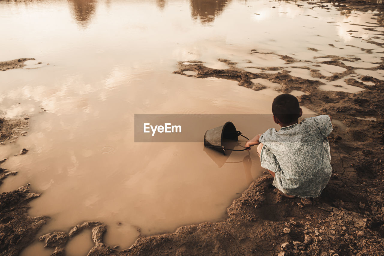 Rear view of boy collecting water from lake in bucket