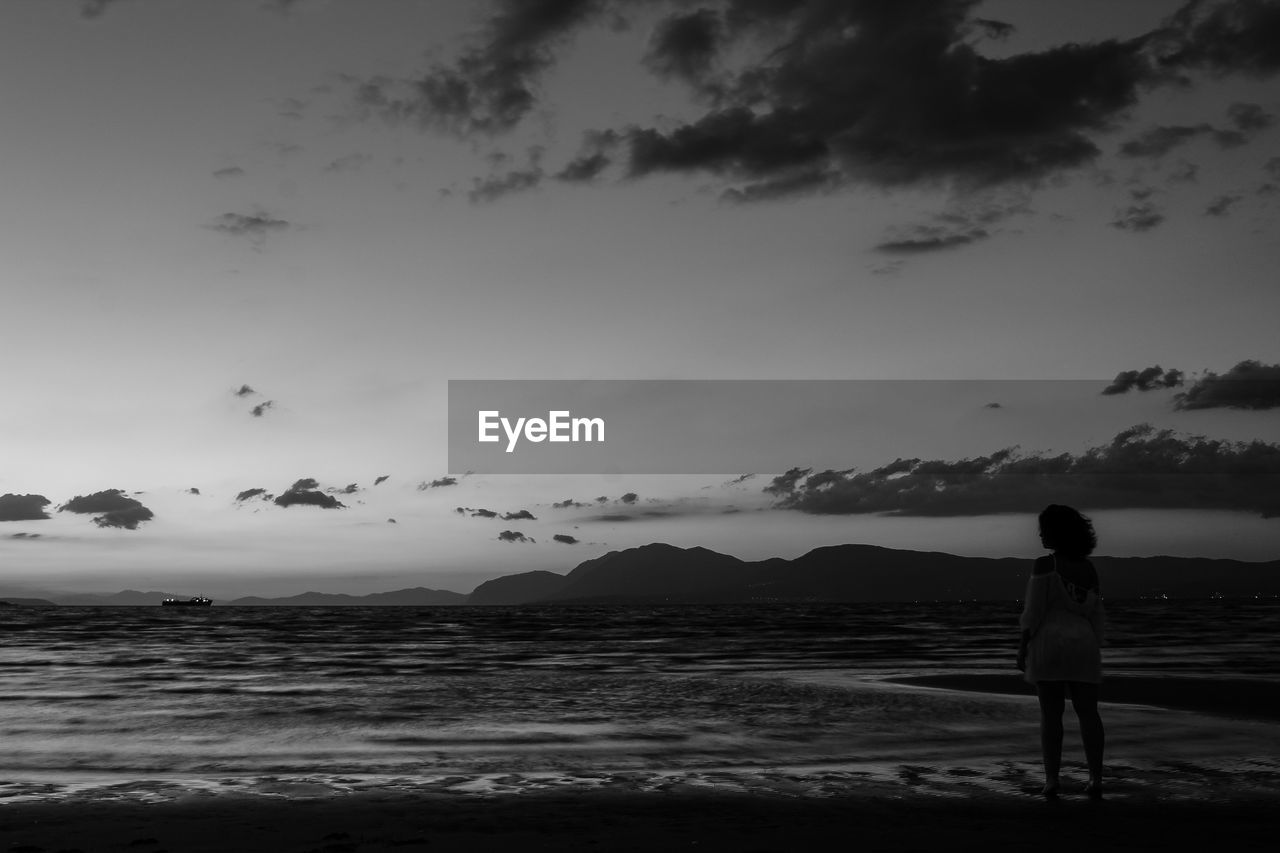 REAR VIEW OF MAN STANDING AT BEACH