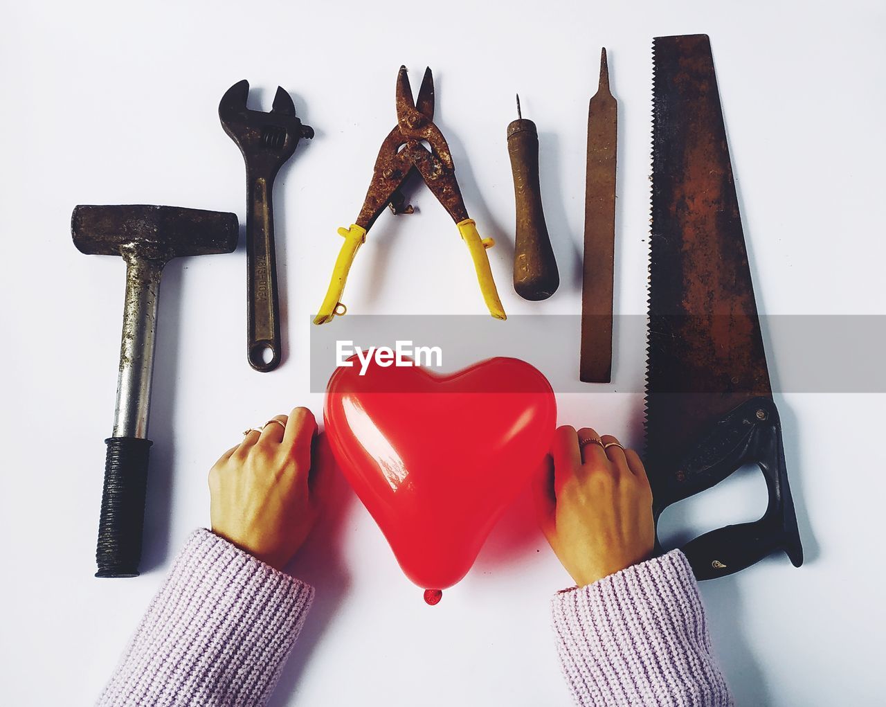 Cropped hands of woman with red heart shape balloon and work tools over white background
