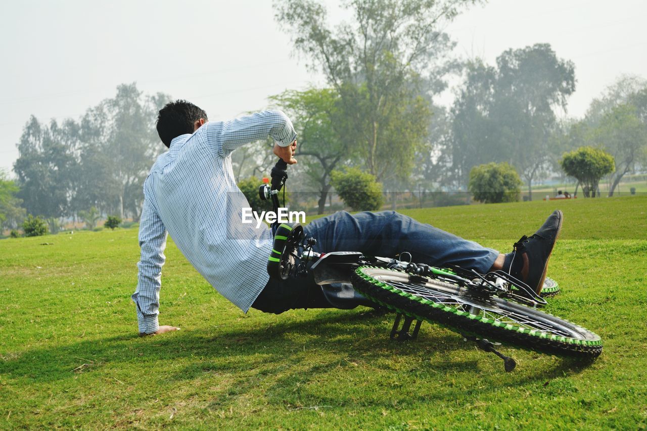 Rear view of man falling from bicycle on grassy field in park