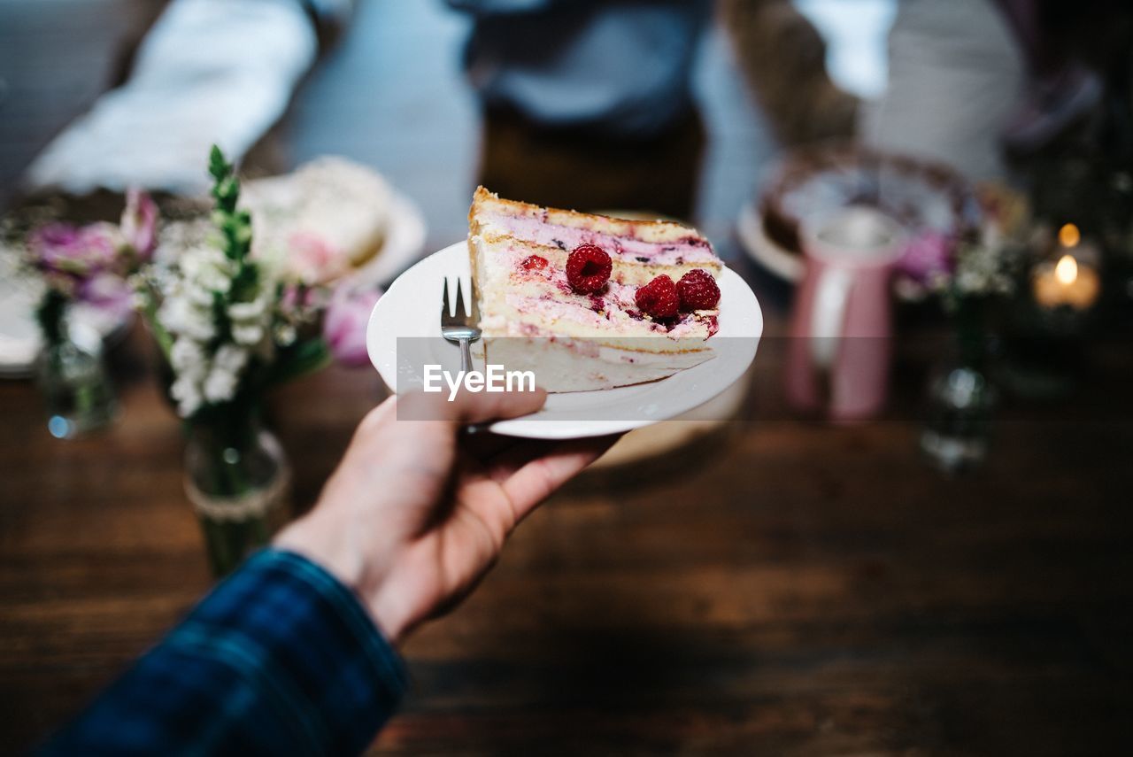 Close-up of cropped hand holding cake slice in plate