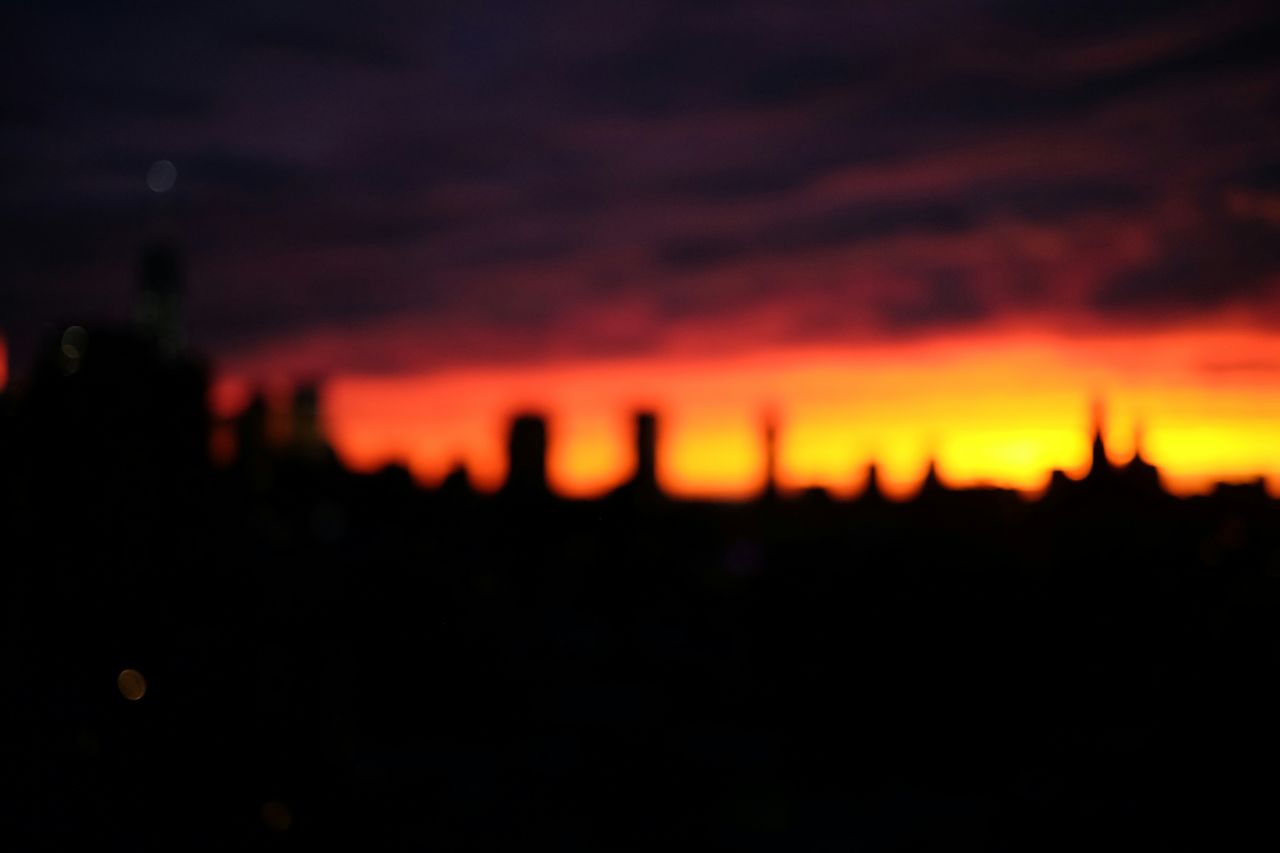 Defocused image of silhouette city against orange cloudy sky