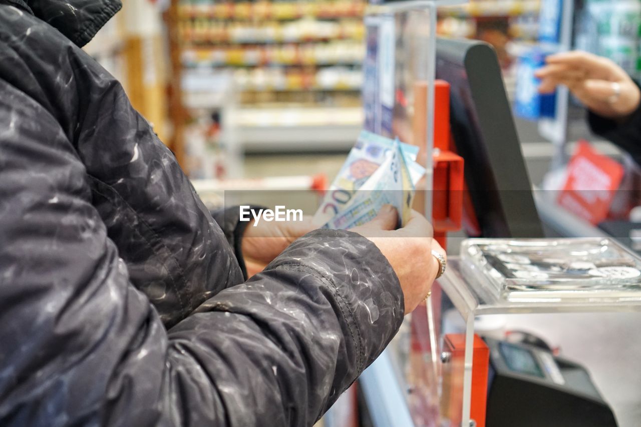 MIDSECTION OF WOMAN HOLDING CAMERA WHILE STANDING BY STORE