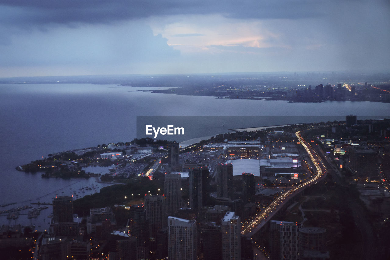 High angle view of illuminated city by sea against sky