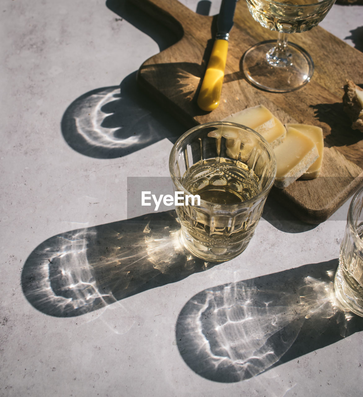 Top view composition with glasses of wine served with sliced cheese and bread with jam on marble table with wooden board in sunlight