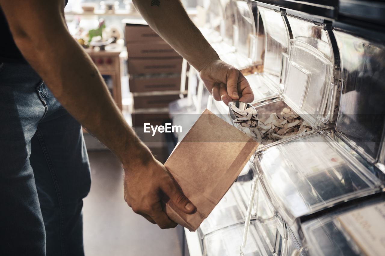 Midsection of male customer filling slice coconut in paper bag at organic store