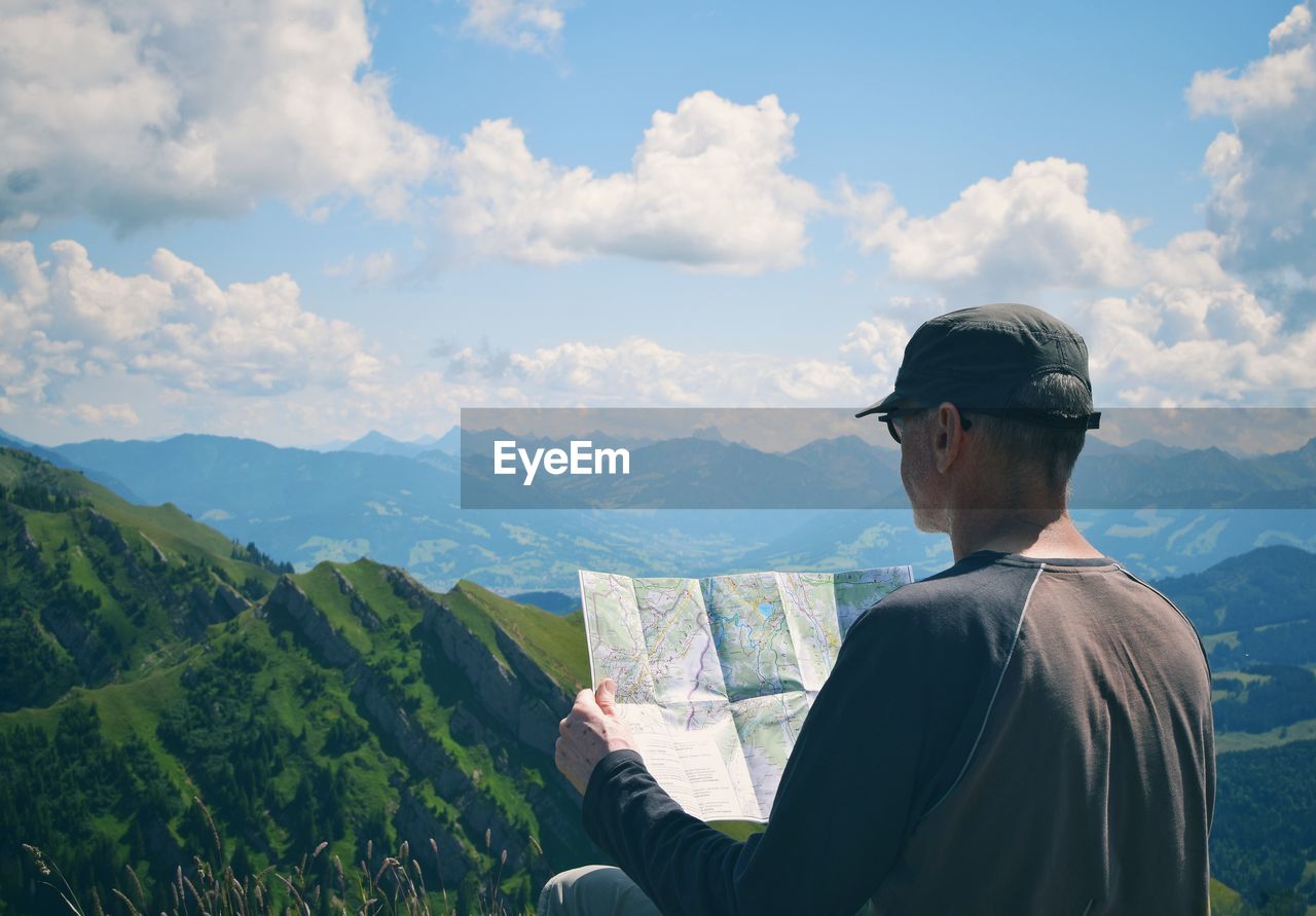 Rear view of man holding map with mountains in background against sky