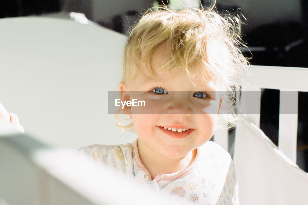 Close-up portrait of cute baby girl smiling in crib at home