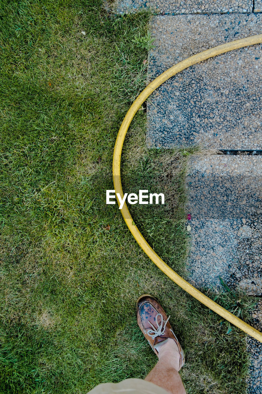 Low section of man standing by yellow garden hose in yard