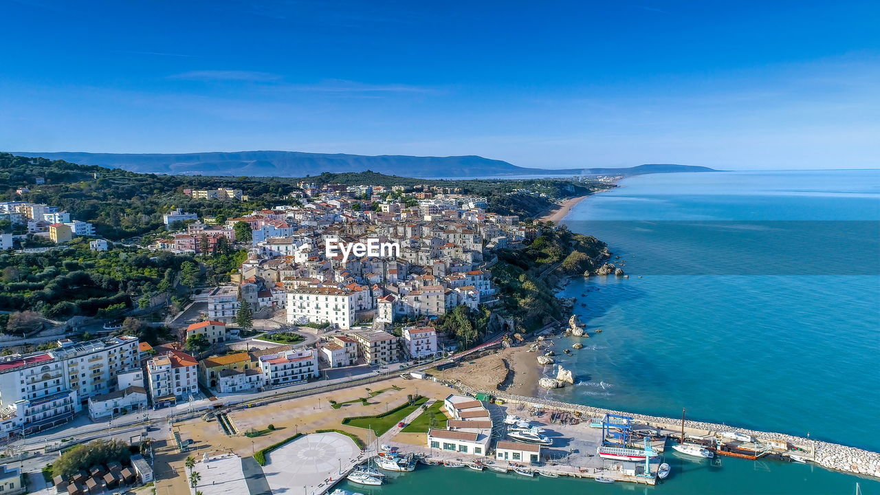 High angle view of townscape by sea against blue sky