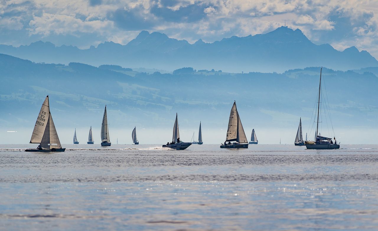 SAILBOATS SAILING IN SEA BY MOUNTAINS AGAINST SKY