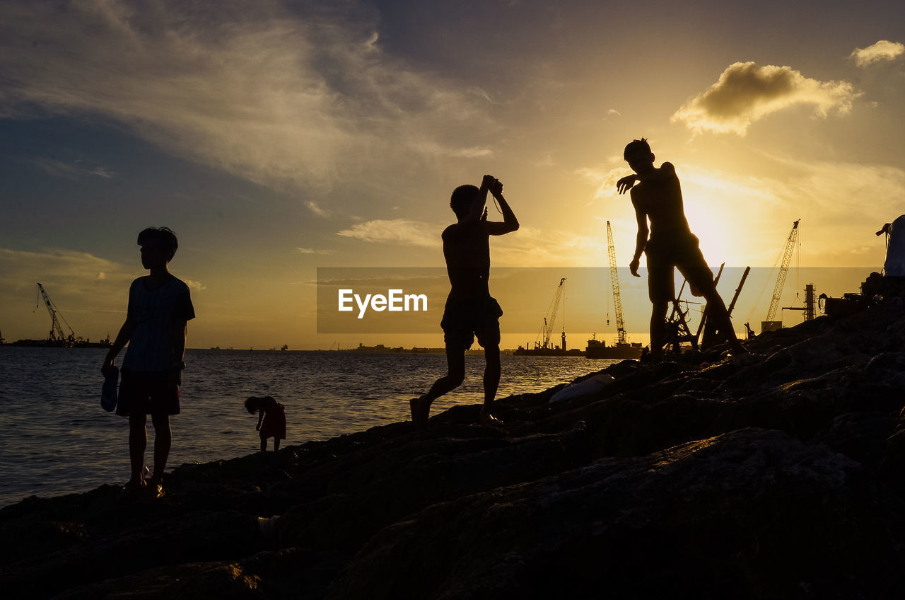 Silhouette people on beach against sky during sunset